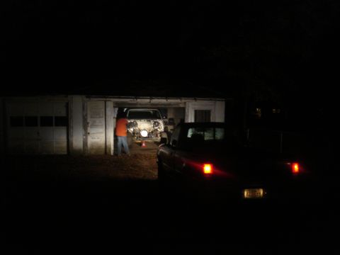 1991 Ford Bronco - A person in an orange shirt and blue jeans stands near the front of a disassembled vehicle in a garage at night. The rear of a red pickup t…