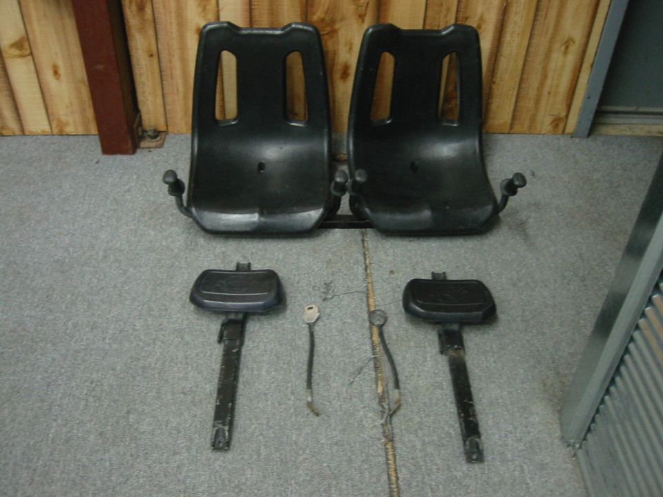 Two black plastic bucket seat shells with pedestal slider rails removed and laid on a shop floor