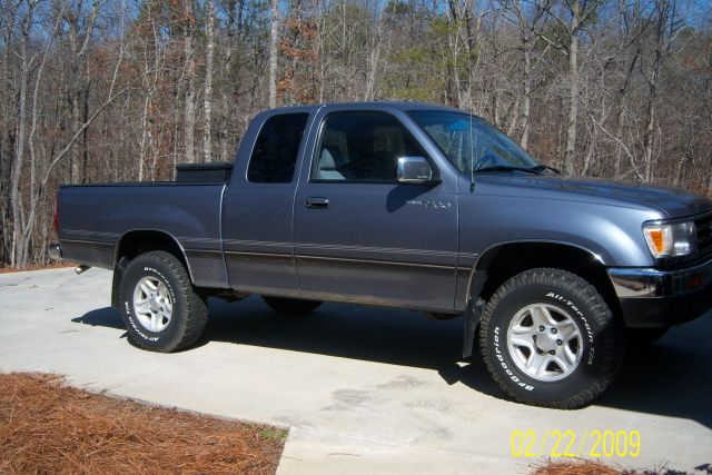 Dark gray Toyota pickup truck with aftermarket wheels and all-terrain tires parked on a concrete driveway.