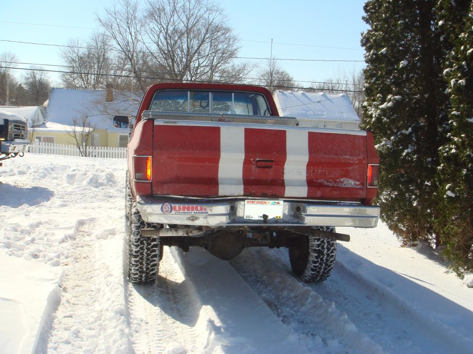 Rear view of a red 1985 Chevrolet C/K pickup truck with white stripes in the snow.