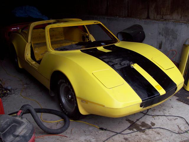 Yellow kit car coupe with black stripe, door off, in a garage