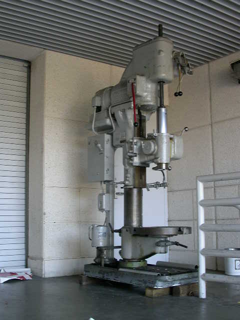 1990 Ford Bronco - A large industrial drill press is shown in a workshop setting. The machine is light gray and appears to be a stationary model.