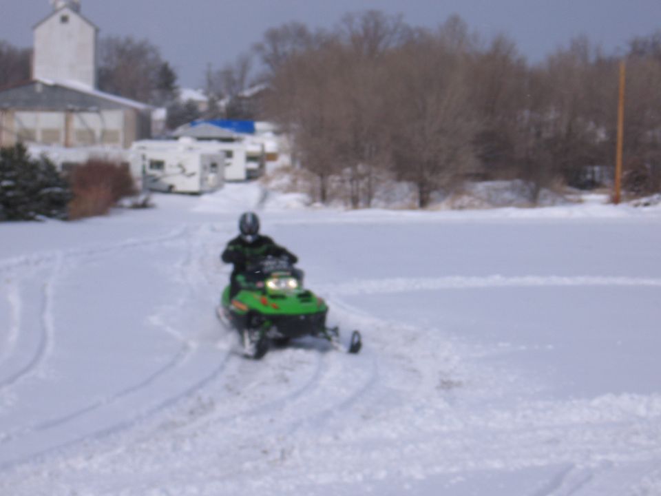 Green snowmobile being ridden across a snowy field