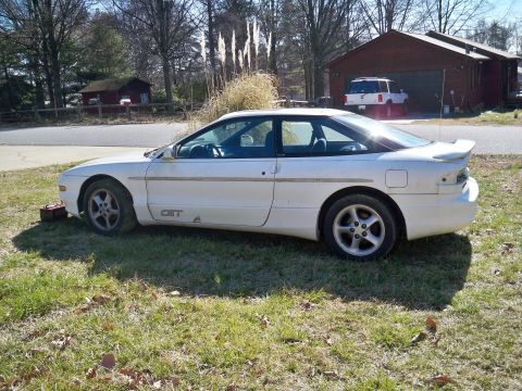 1995 Ford Probe - The side profile of a white Ford Probe GT is parked on a grassy lawn in front of a residential building and a detached garage. A red toolbo…