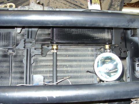 1988 Ford Bronco - A black transmission cooler is mounted in front of the radiator of a 1988 Ford Bronco. A round fog light is also visible below the cooler.