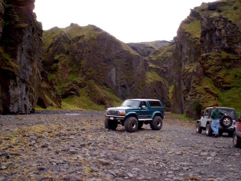 1996 Ford Bronco - Two SUVs are parked on a rocky surface within a narrow canyon with moss-covered cliffs.