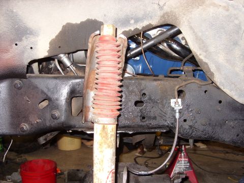 1988 Ford Bronco - A close-up view of the underside of a vehicle's frame, showing a shock absorber with a red bellows, brake lines, and part of the exhaust sy…