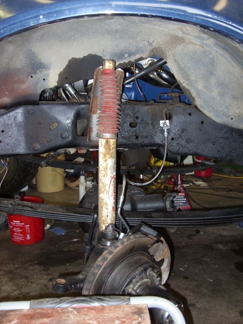 1988 Ford Bronco - A close-up view of the front suspension and brake assembly of a vehicle, likely a 1988 Ford Bronco, showing a shock absorber, leaf springs,…