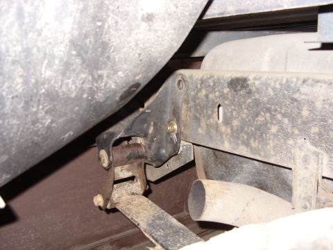 1988 Ford Bronco - The underside of a vehicle shows a black metal bracket attached to the frame, supporting a rusty leaf spring. A portion of a large cylindri…