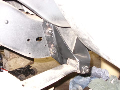 1988 Ford Bronco - A close-up view of the underside of a vehicle frame, showing a black metal bracket bolted to the frame with two bolts. A hydraulic jack and…
