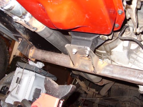 1988 Ford Bronco - Underneath view of a modified exhaust system and transmission crossmember bolted to a vehicle frame. A red transmission pan is visible abov…