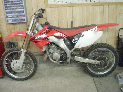 2005 Honda CR125R - A red and white Honda dirt bike is parked indoors, possibly in a garage or workshop.