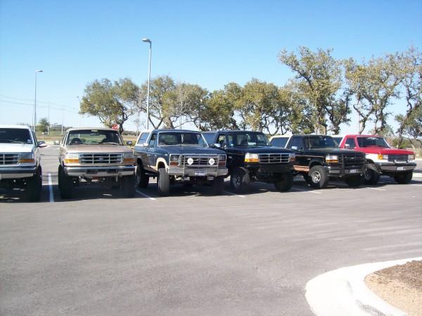 Several lifted Ford trucks and an SUV parked in a lot.