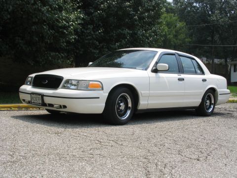 1998 Ford Crown Victoria - A white 1998 Ford Crown Victoria sedan is parked on an asphalt surface with trees in the background.