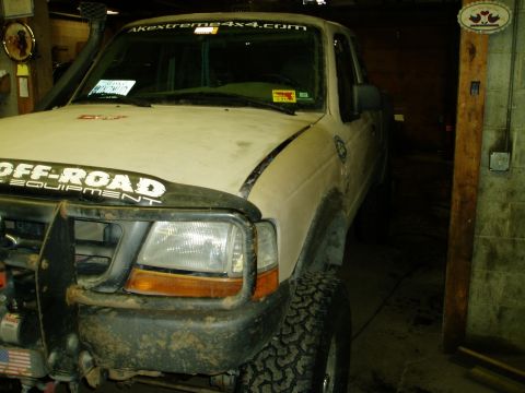 2000 Ford E350 - A white Ford pickup truck with off-road modifications is parked in a garage. The front of the truck features a brush guard, large headlight…