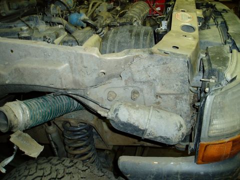 2000 Ford E350 - The front driver's side frame rail of a Ford E350 shows significant rust and damage, with a green ribbed hose and suspension components vis…