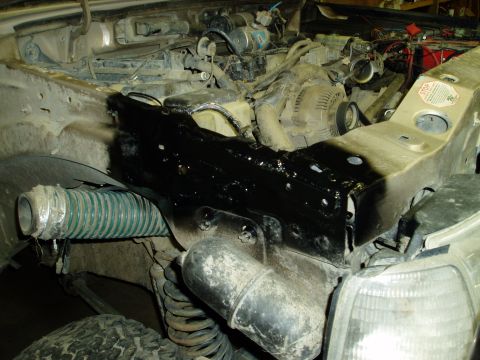 2000 Ford E350 - The engine bay of a vehicle shows a black-painted metal component that appears to be a newly installed or repaired part, possibly a frame r…