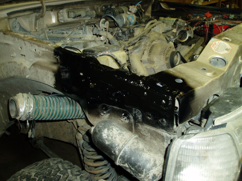 Engine bay with black painted part, green hose, engine, and headlight.