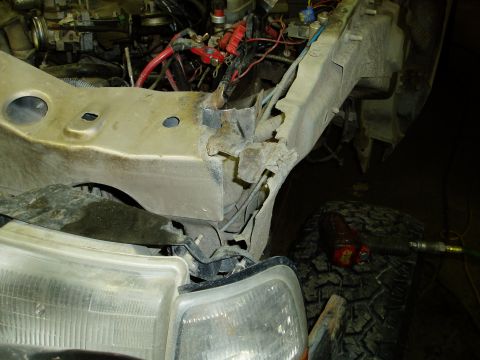 2000 Ford E350 - Close-up view of the rusted and damaged front frame rail and surrounding engine bay components of a Ford E350 van. The headlight assembly a…