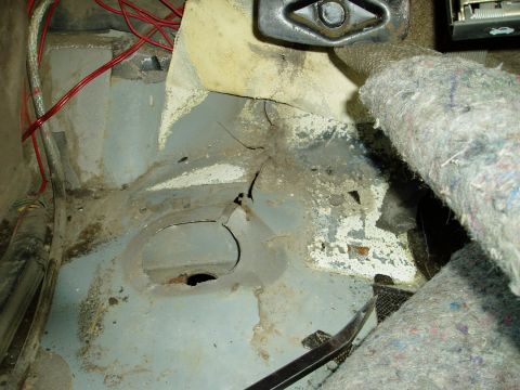 2000 Ford E350 - The interior floor of a vehicle shows significant rust and damage, with exposed wiring and a large hole in the metal. A crowbar is visible…