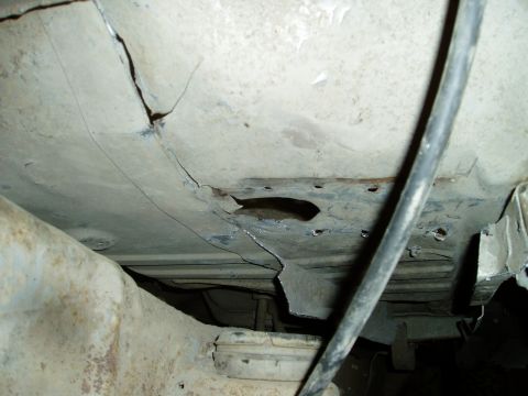 2000 Ford E350 - The underside of a vehicle shows significant rust and damage, with a large hole and cracks in the metal body. A black cable runs diagonally…