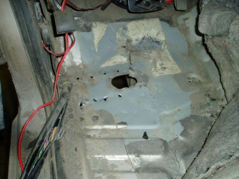 2000 Ford E350 - The interior floor of a vehicle shows rust and damage, with exposed wiring and a hole in the metal floor pan. A black conduit with colorful…