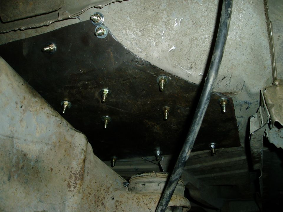 Underside view of a vehicle frame with a custom metal reinforcement plate and bolts.