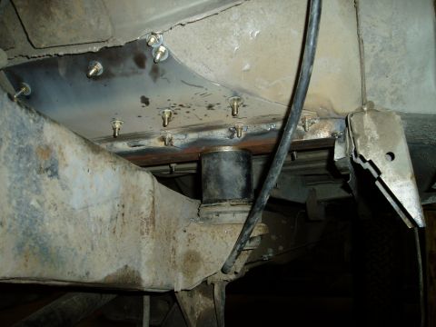 2000 Ford E350 - A close-up view shows a metal plate bolted to the underside of a vehicle's frame, with a rubber bushing visible between the frame and anoth…