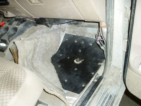 2000 Ford E350 - The interior floor of a vehicle shows a black metal plate installed over the carpet, secured with multiple screws. Various wires are visibl…