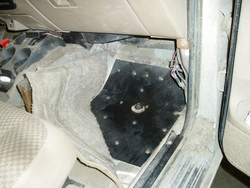 Interior of a vehicle showing a black metal floor plate with screws and visible wiring.