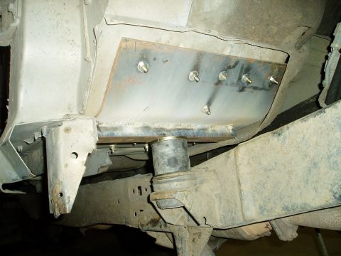 2000 Ford E350 - A close-up view of the undercarriage of a vehicle, showing a metal plate bolted to the frame with multiple bolts. A rubber bushing is visib…