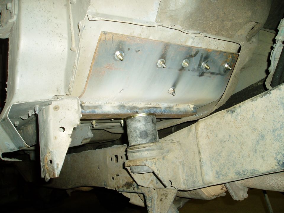 Undercarriage of a vehicle showing a bolted metal plate and a rubber bushing.