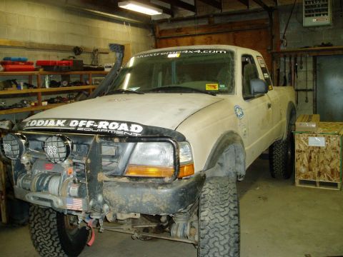 2000 Ford E350 - A tan Ford Ranger pickup truck is parked in a garage with a winch and KC lights mounted on the front bumper. The truck has a snorkel on the…