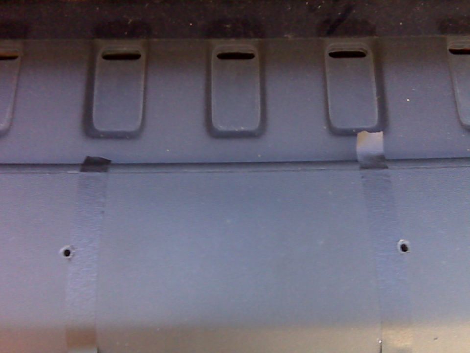 Close-up of textured plastic exterior with recessed slots and holes, secured with tape.