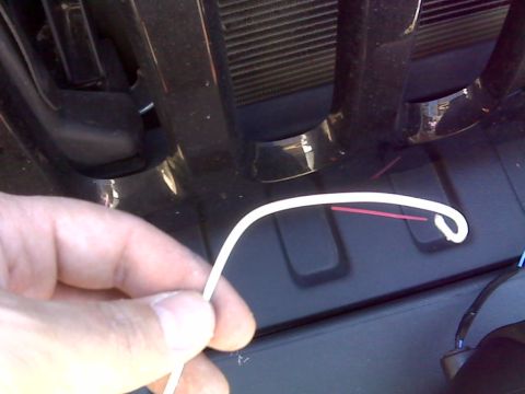 2008 Jeep Wrangler - A hand holds a white wire with a red wire inside it, near the front grille of a dark-colored vehicle.