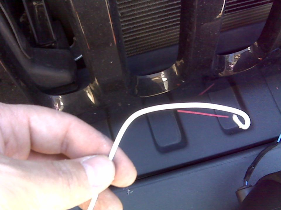 Hand holding white wire with red wire inside near black Jeep Wrangler grille.