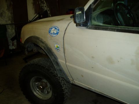 2000 Ford E350 - The side view of a light-colored Ford truck is shown, with a large tire and fender well in the foreground. Two stickers are visible on the…