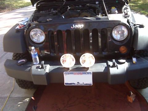 2008 Jeep Wrangler - The front of a black Jeep Wrangler is shown with its hood open, revealing the engine bay. Two round auxiliary lights are mounted on the fro…