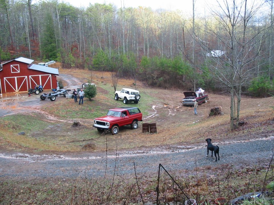 Lifted red and black Ford Bronco SUV parked on muddy lot near a red barn