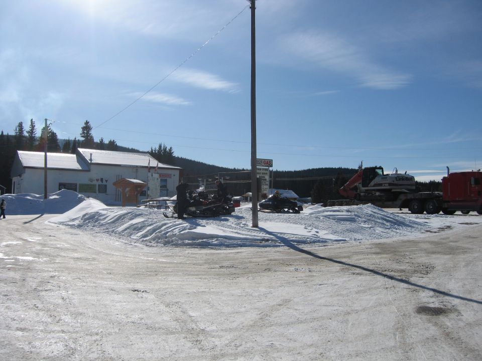 Snowmobile parked in snow with building and gas station sign.