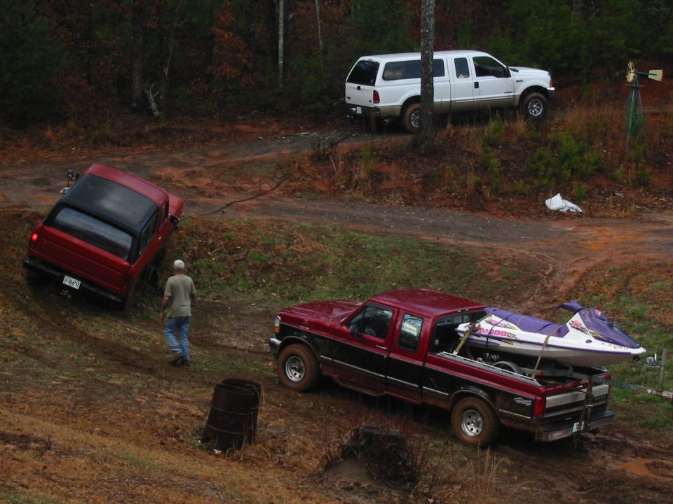 Red pickup, white truck and jet skis on a muddy trail in the woods