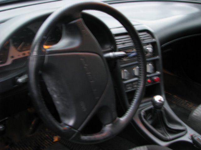 Blurry interior view of black steering wheel, center console and manual shifter in a Ford Probe
