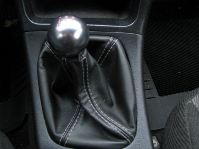 Round metal shift knob on black leather shift boot with white stitching on car center console