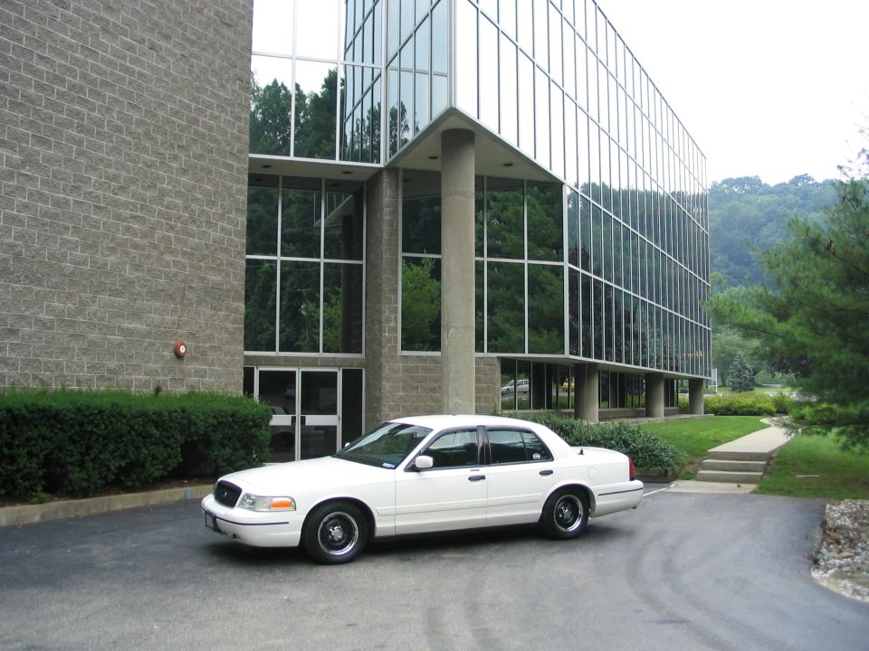 White 1998 Ford Crown Victoria parked in front of a modern glass building
