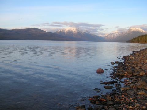 1996 Ford Bronco - A serene lake with mountains in the background, reflecting the sky and clouds. The foreground shows a rocky shoreline with clear water.