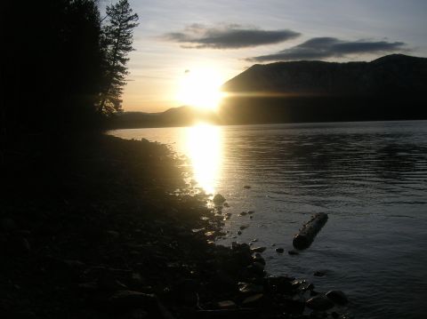 1996 Ford Bronco - A serene lake scene at sunset with the sun reflecting on the water. Silhouetted trees and mountains frame the tranquil landscape.
