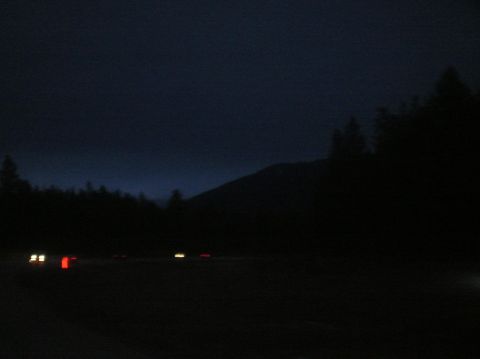 1996 Ford Bronco - The headlights and taillights of several vehicles are visible on a dark road at dusk or night. A dark, silhouetted treeline and a mountain…