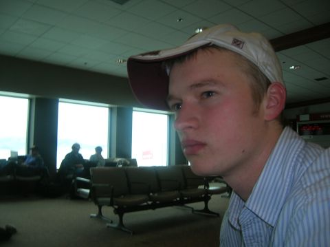 1996 Ford Bronco - A young man wearing a white baseball cap and a striped shirt is in the foreground, looking to the right. In the background, people are sitt…