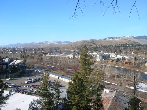 1996 Ford Bronco - A wide shot of a town nestled in a valley with mountains in the background. A river flows through the center of the town, with buildings an…