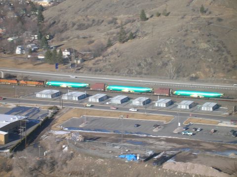 1996 Ford Bronco - An aerial view captures a train carrying large, cylindrical, green cargo containers on flatbed rail cars, moving alongside a highway and a…